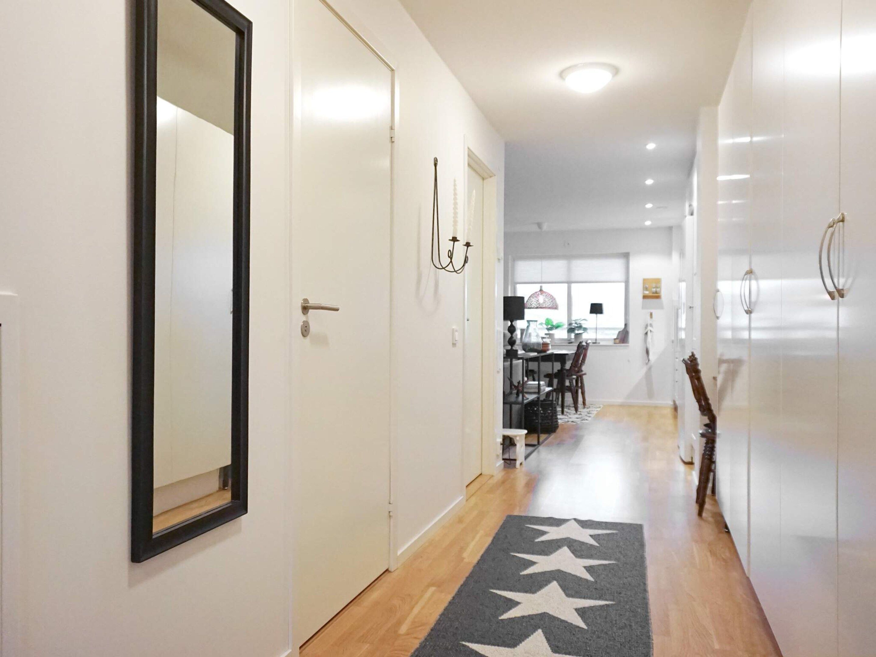 A hallway with a mirror, a star-patterned rug, and a dining area in the background.