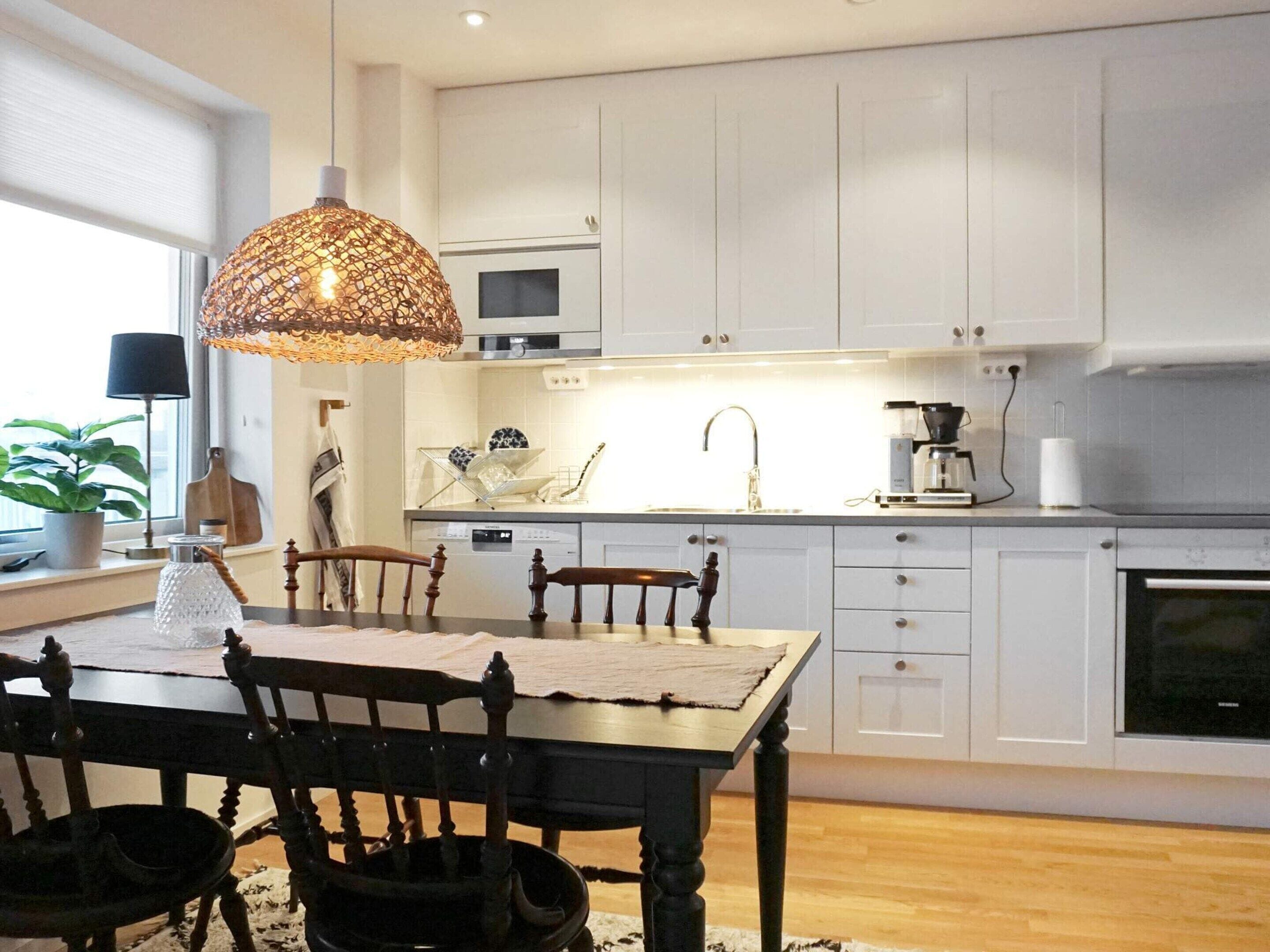 Une cuisine moderne avec des meubles blancs, une table à manger en bois et un luminaire suspendu.