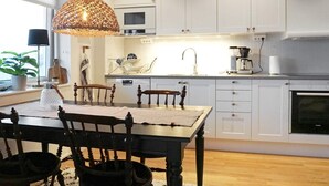 A modern kitchen with white cabinets, a wooden dining table, and a hanging light fixture.