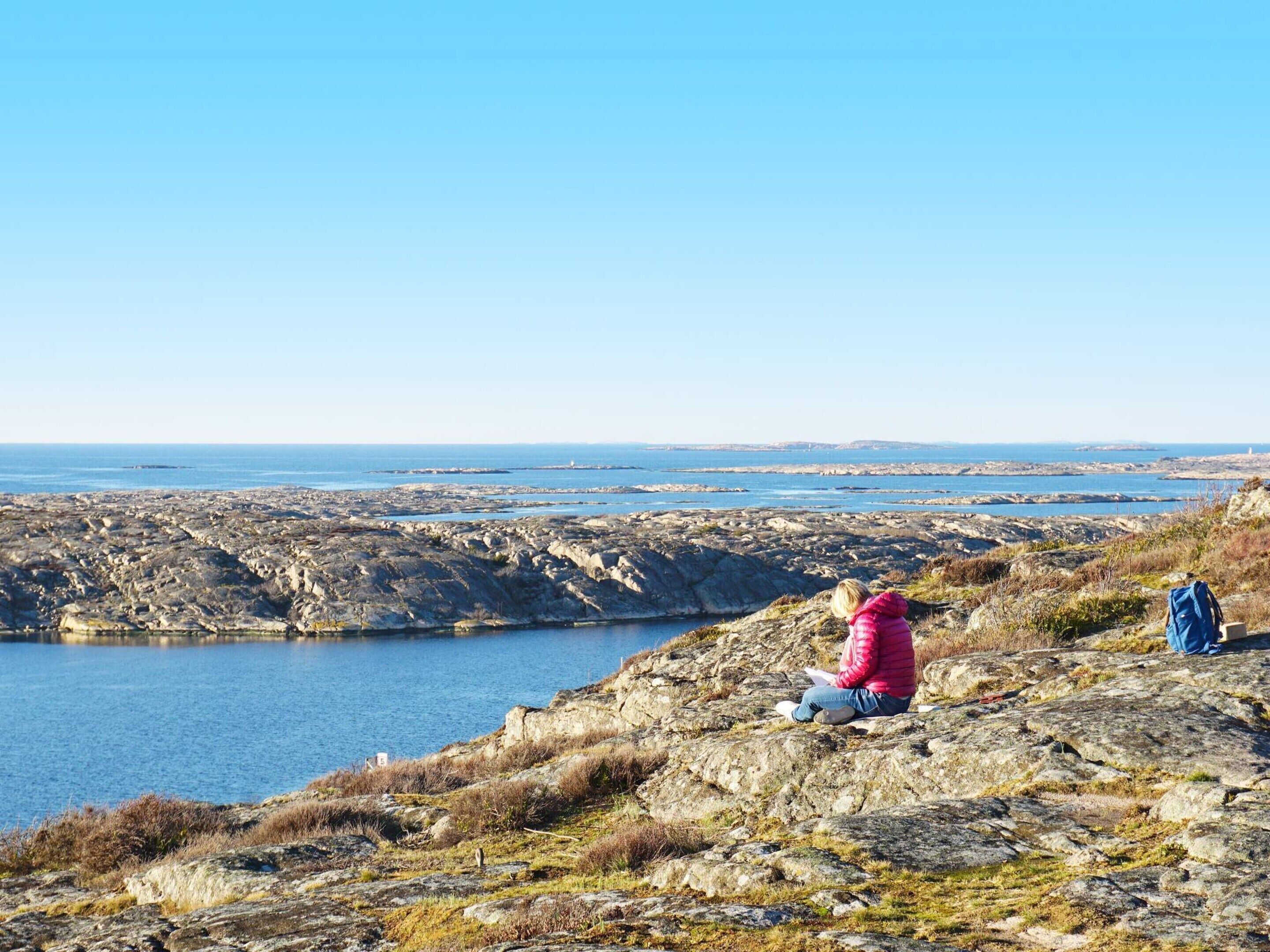 A person sitting on a rocky outcrop overlooking a body of water with a clear sky.