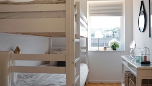 A bedroom with bunk beds, a small window with a view, a desk with a mirror, and a vase with flowers.