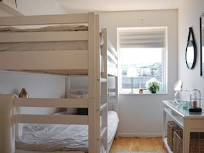 A bedroom with bunk beds, a small window with a view, a desk with a mirror, and a vase with flowers.