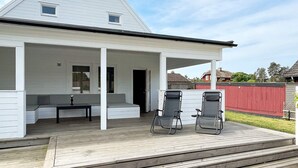 A house with a covered porch, two lounge chairs, and a small table. - 4 Star Holiday Home in Kopingsvik (Kopingsvik)