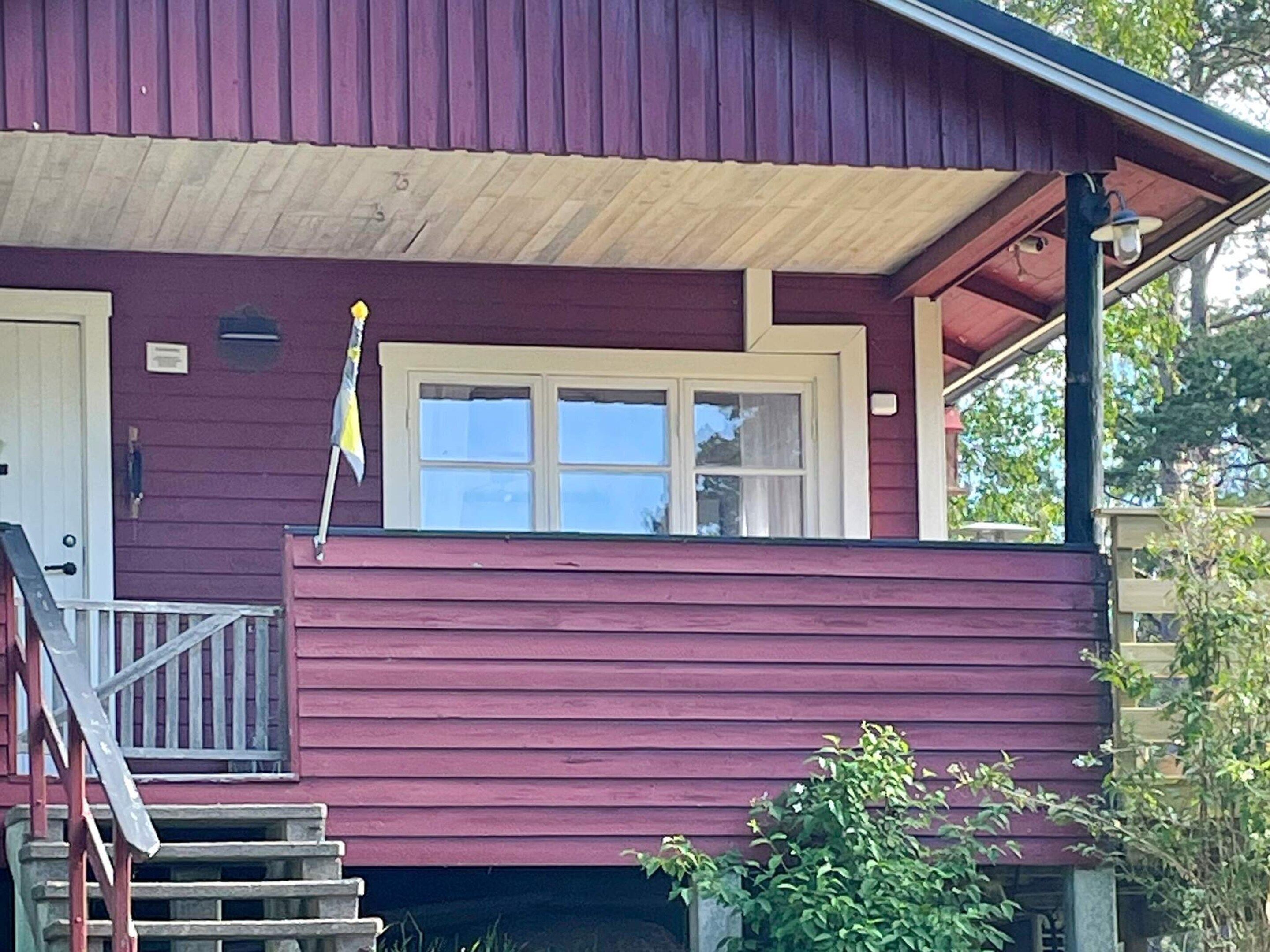 Ein zweistöckiges Haus mit roter Fassade, einer Haustür und einem Fenster mit einer Flagge.
