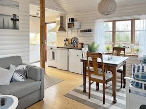 A modern kitchen with white cabinetry, a dining area with a wooden table and chairs, and a grey sofa. - 4 Person Holiday Home in Nynashamn (Nynashamn)