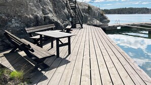 Eine hölzerne Steg, der sich über ein Gewässer erstreckt, mit Bänken und einer Treppe, die zu einer felsigen Klippe hinaufführt.