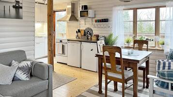 A modern kitchen with white cabinetry, a dining area with a wooden table and chairs, and a grey sofa.