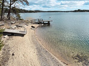 A lakeside beach with a wooden dock and seating area. - 4 Person Holiday Home in Nynashamn (Nynashamn)