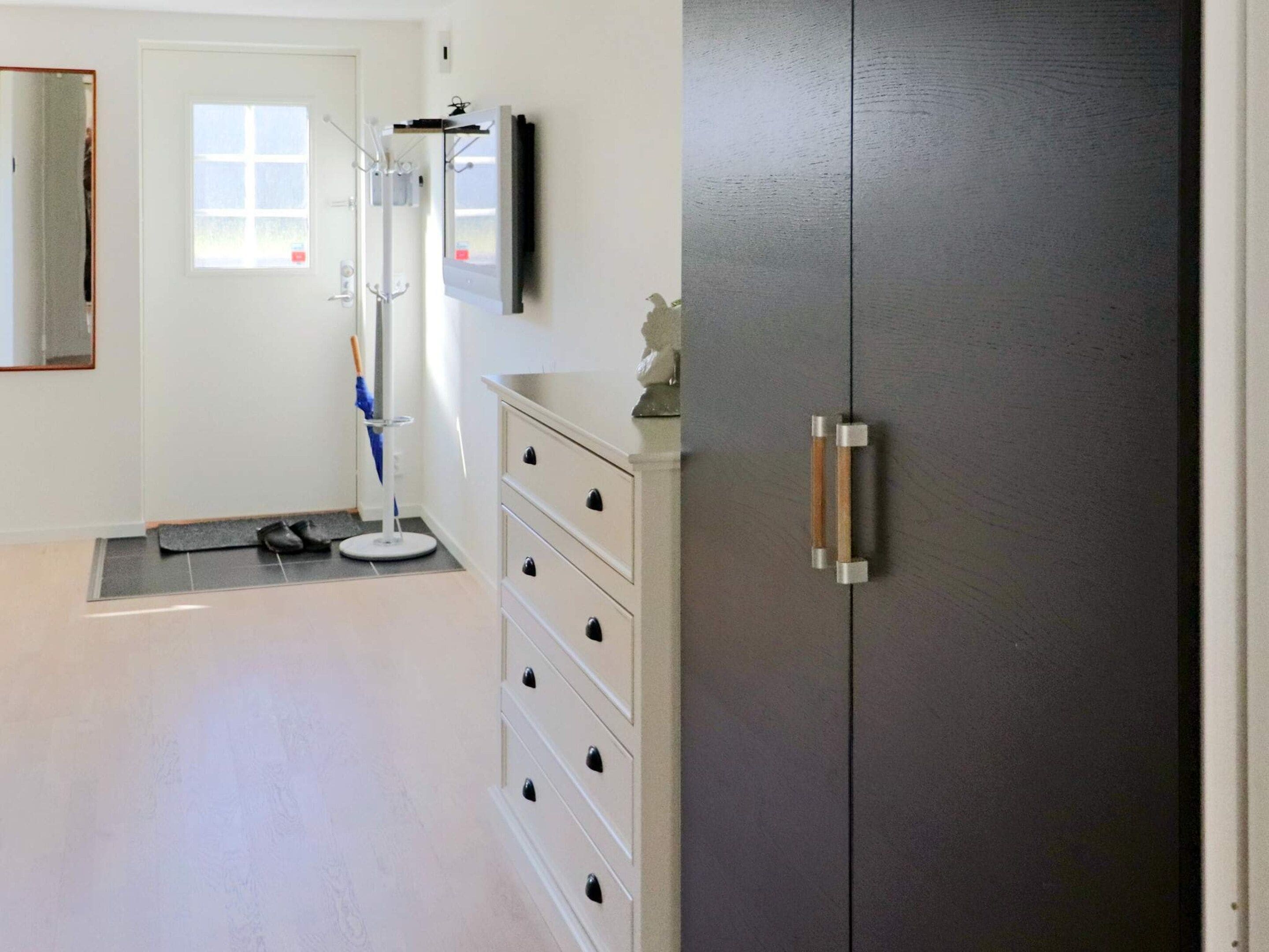 A room with a white dresser, a dark wardrobe, a window, and a door.