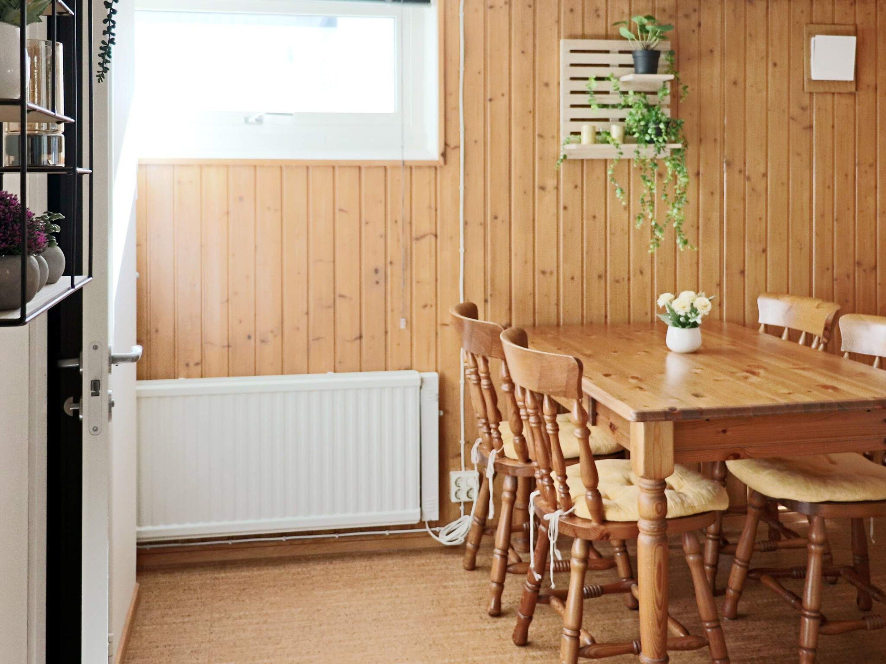 A dining area with a wooden table and chairs, a white radiator, and a window with blinds.