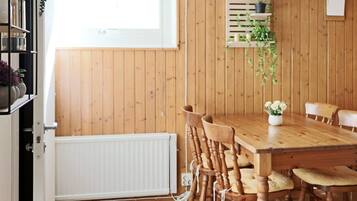 A dining area with a wooden table and chairs, a white radiator, and a window with blinds.