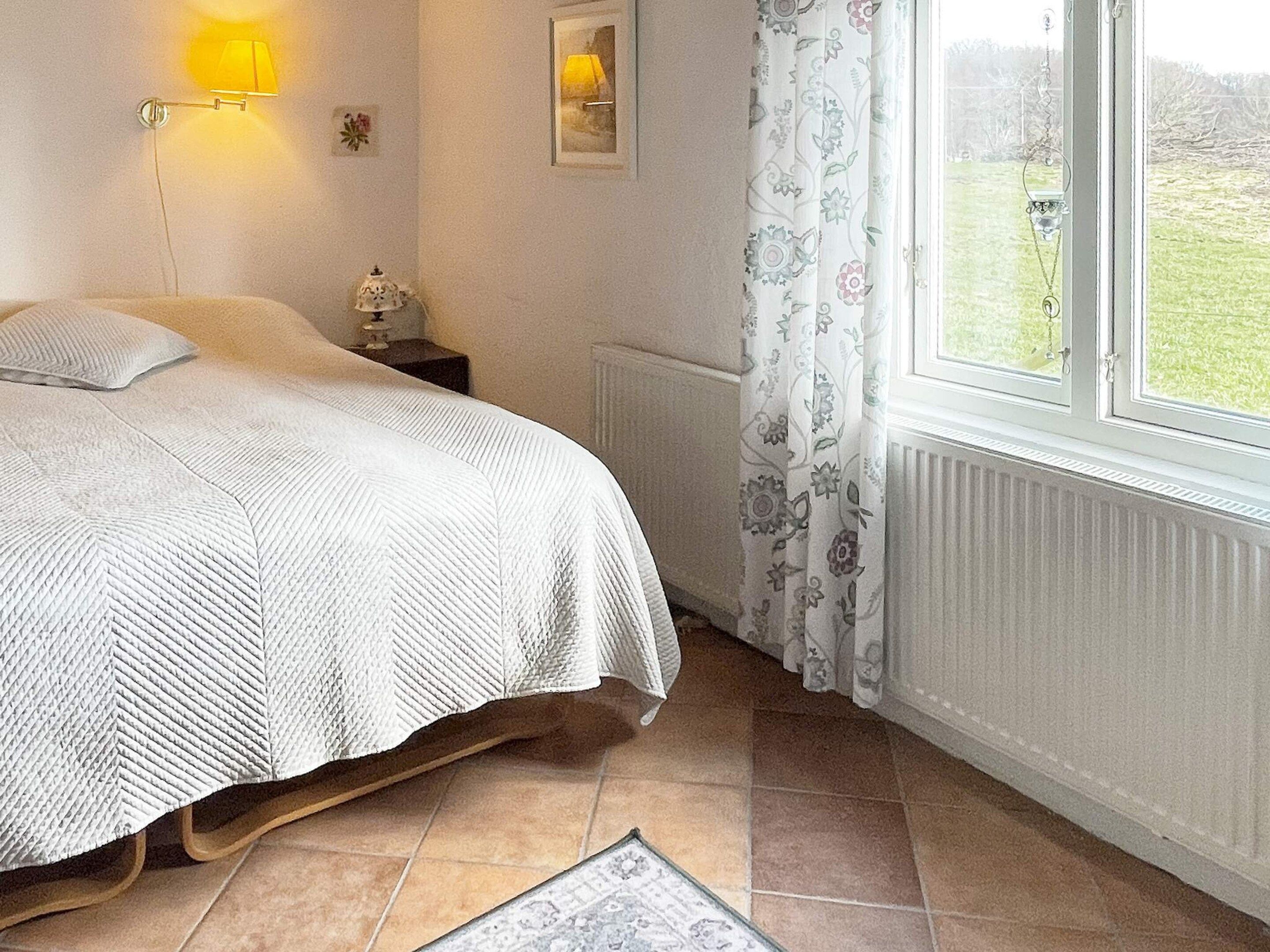 A bedroom with a bed, a nightstand, a lamp, a radiator, and a window with curtains.