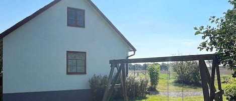 Ett vitt hus med ett sadeltak, en gunga och en gräsklädd trädgård.