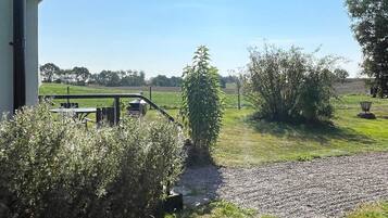 A view from a window overlooking a gravel path leading to a grassy area with a bench and a picnic table.