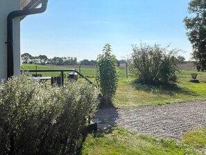 Vista desde una ventana a un sendero de grava que conduce a una zona verde con un banco y una mesa de picnic.
