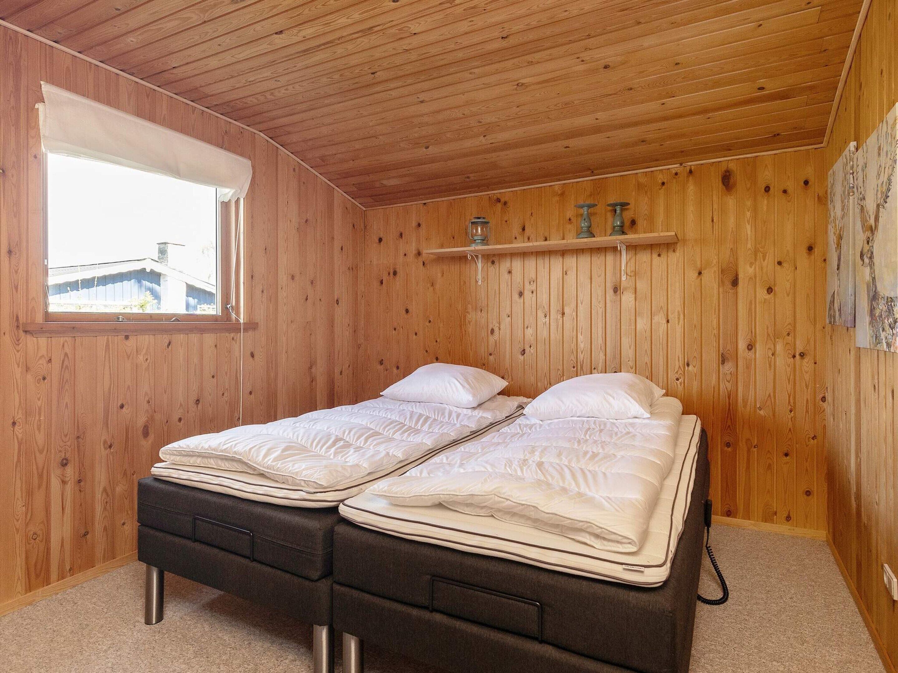 Una habitación con paneles de madera, una cama, una ventana y una estantería con adornos.