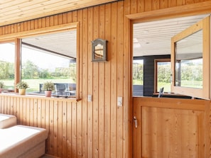 A wooden-paneled room with a bed, a window with a view of greenery, and a door with a mirror. - 6 Person Holiday Home in Hadsund (Hadsund)