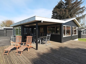 A covered outdoor seating area with wooden chairs and a table, adjacent to a building with large windows. - 6 Person Holiday Home in Hadsund (Hadsund)