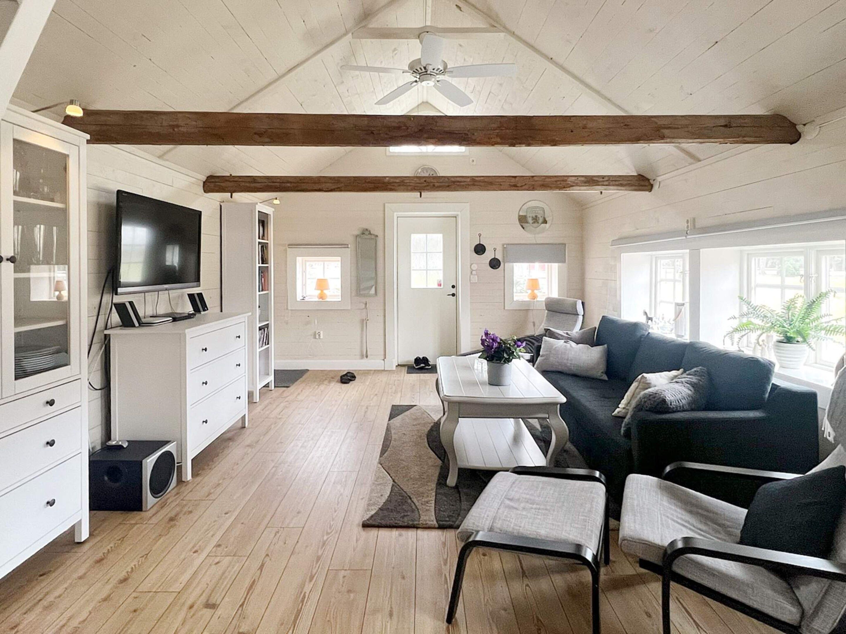 A spacious living area with a ceiling fan, a television, a sofa, a coffee table, and a dining table.