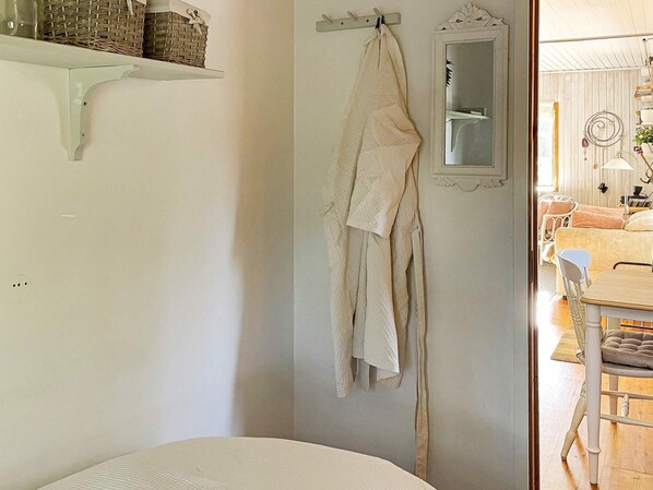 A room with a bed, a hanging robe, a mirror, and a shelf with baskets.