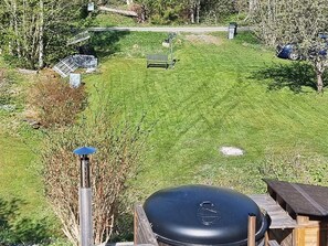 A well-maintained grassy yard with a wooden deck, a barbecue grill, and a bench.