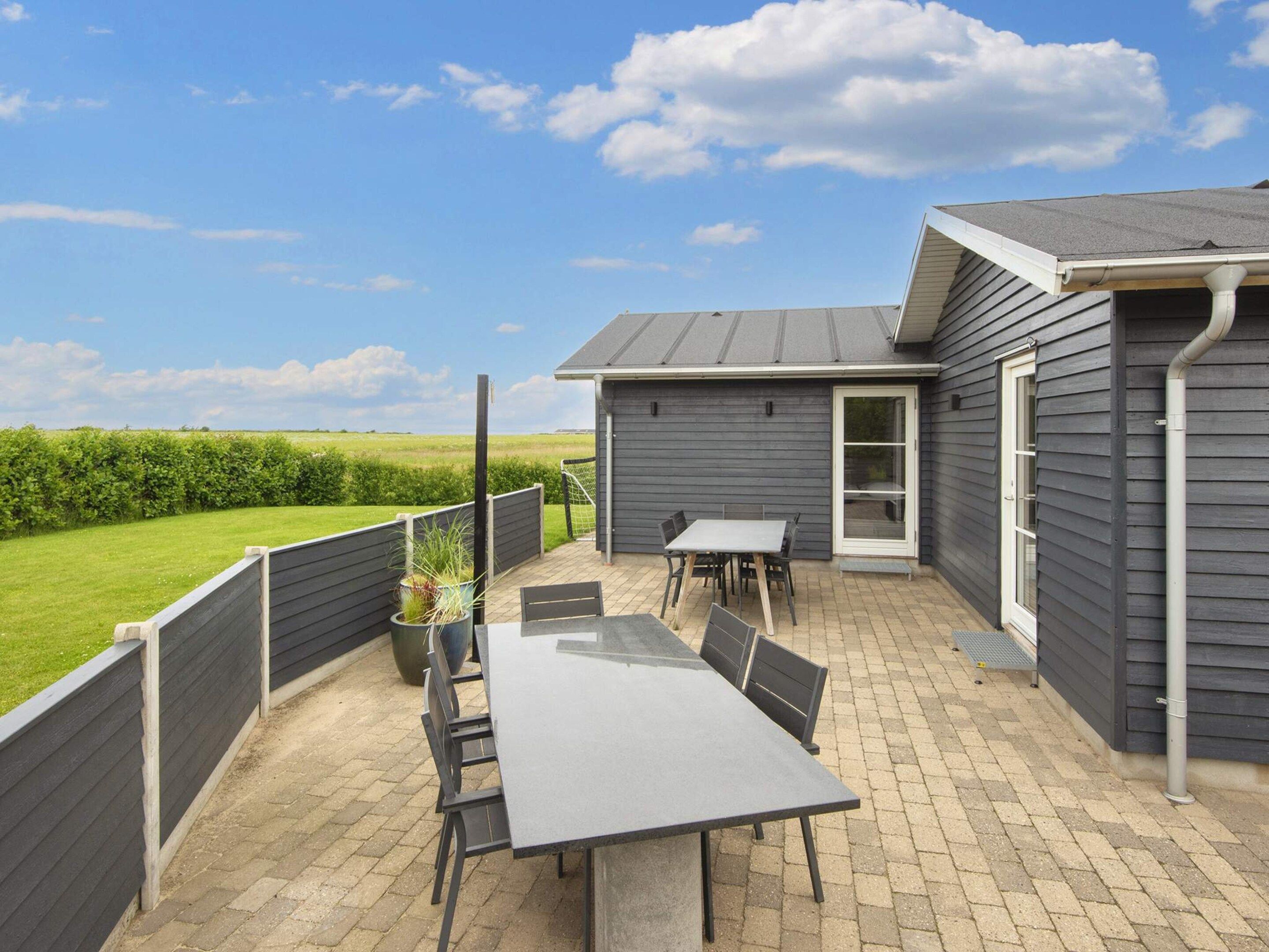 A patio with a table and chairs, a door leading to a covered area, and a view of a green field.