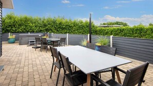 An outdoor patio with a table and chairs, surrounded by a low wall and greenery.