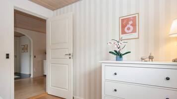 A room with a white dresser, a door, and a hallway leading to another room.