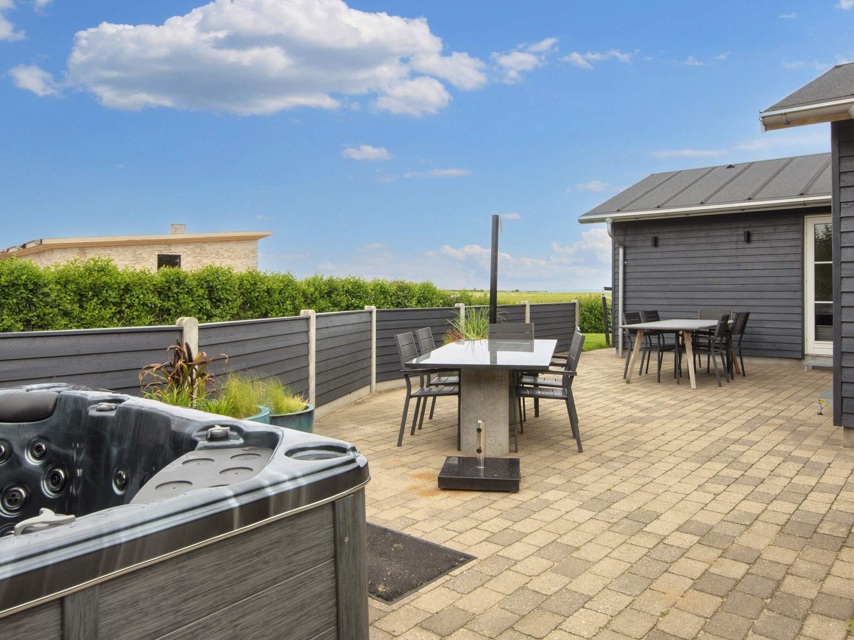 Un patio al aire libre con un jacuzzi, una mesa con sillas y un edificio de fachada oscura.