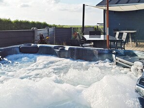 A hot tub with a wooden deck and outdoor furniture.
