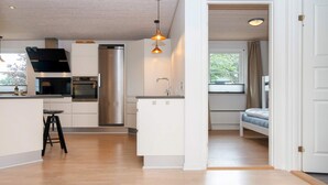 A modern kitchen with a central island, a dining area with a bench, and a bedroom with a window.