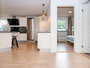 A modern kitchen with a central island, a dining area with a bench, and a bedroom with a window. - 5 Star Holiday Home in Vinderup (Vinderup)