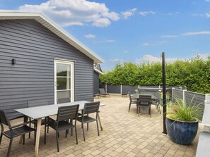 A patio with a table and chairs, a potted plant, and a view of a hedge. - 5 Star Holiday Home in Vinderup (Vinderup)