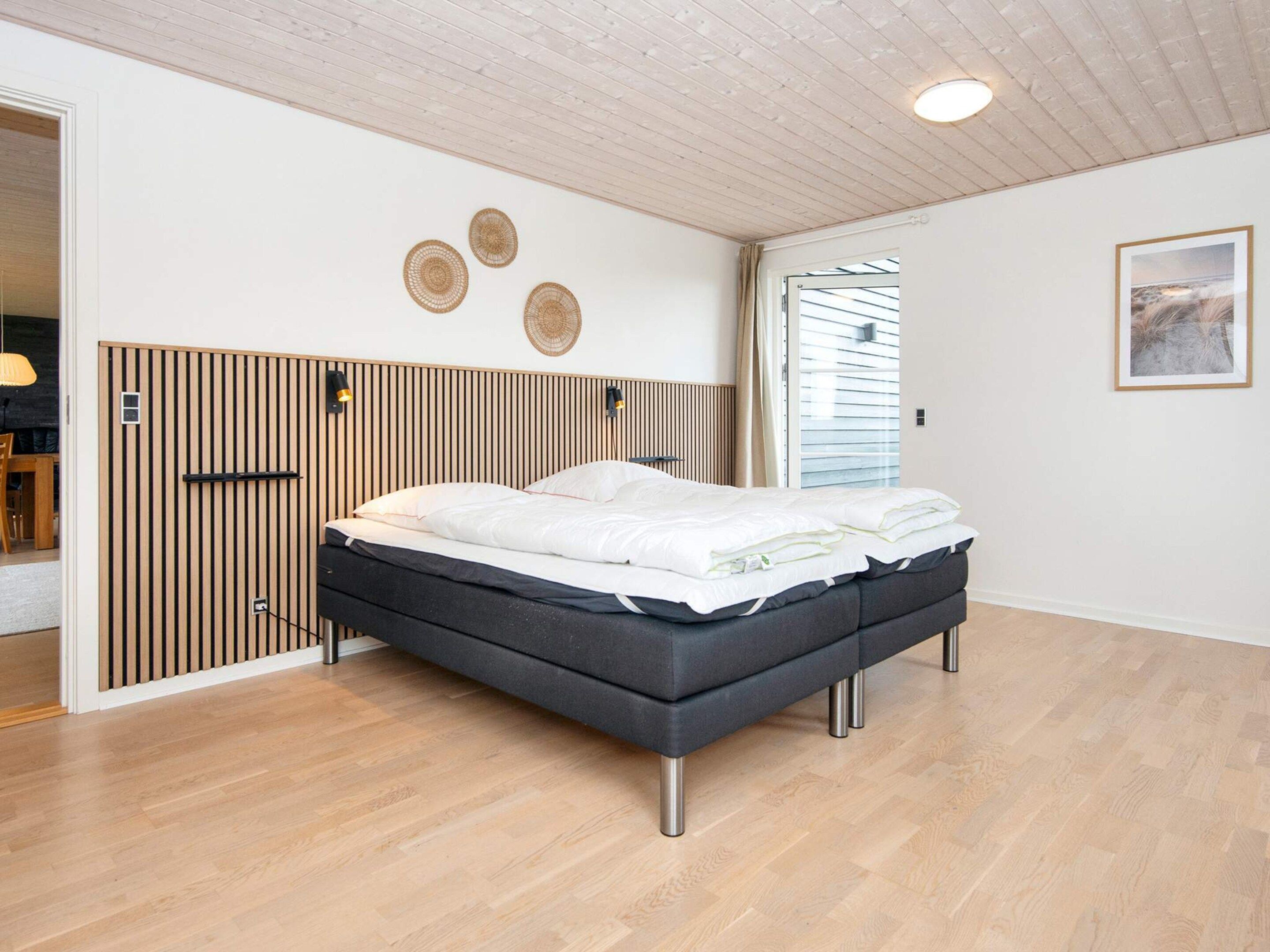 A modern bedroom with a bed, wooden slat headboard, and a window with blinds.