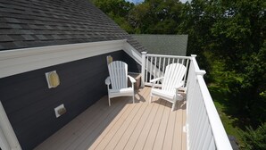 Une terrasse couverte avec deux chaises Adirondack blanches et une balustrade blanche.