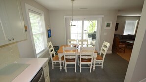 Une cuisine compacte avec un coin repas, comprenant une table et des chaises en bois, un lave-vaisselle et une fenêtre avec des stores.