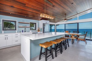 A modern kitchen with a large island, wooden stools, and a view of the ocean.