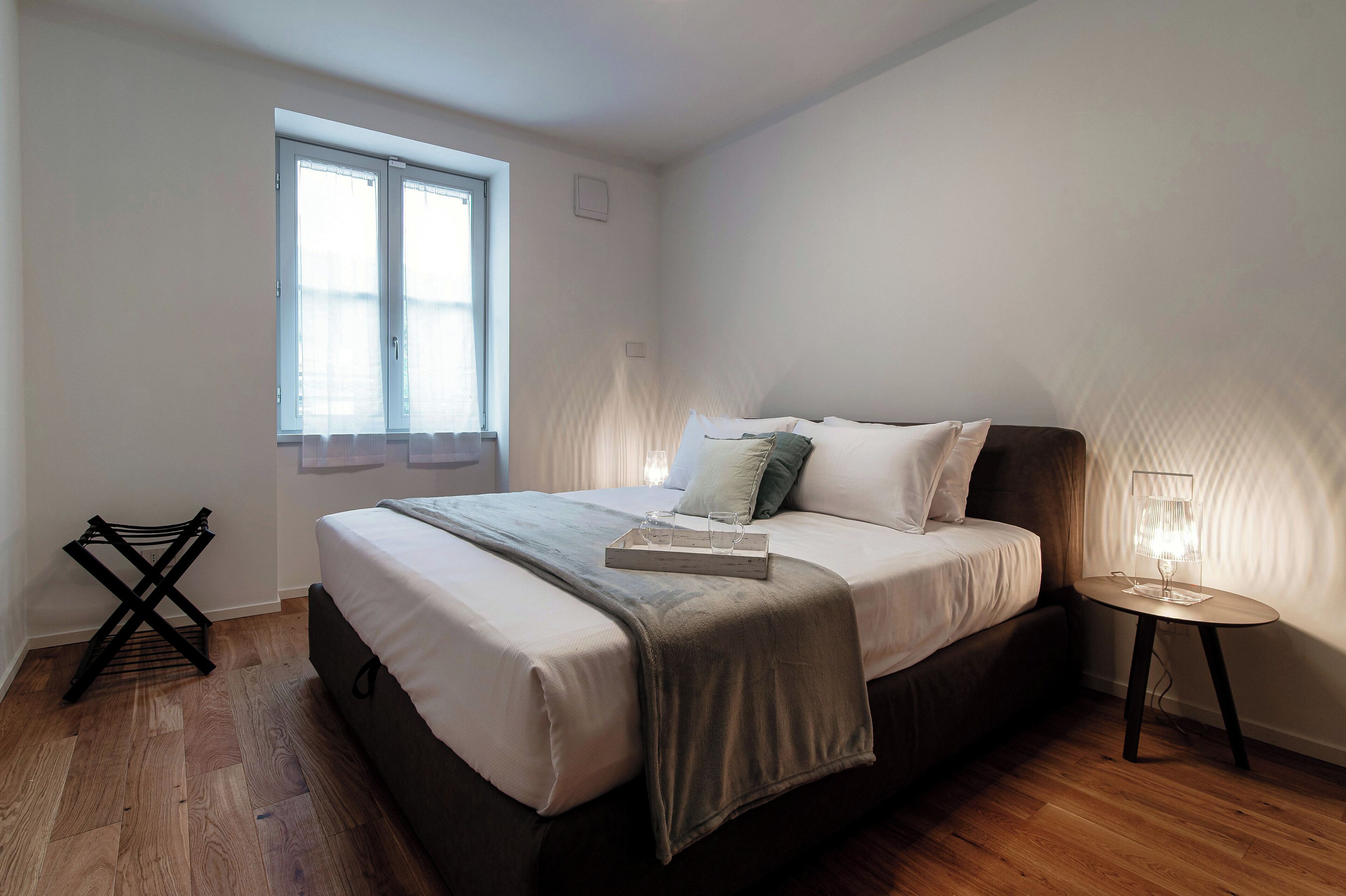Un dormitorio con cama, lámpara de noche y ventana.