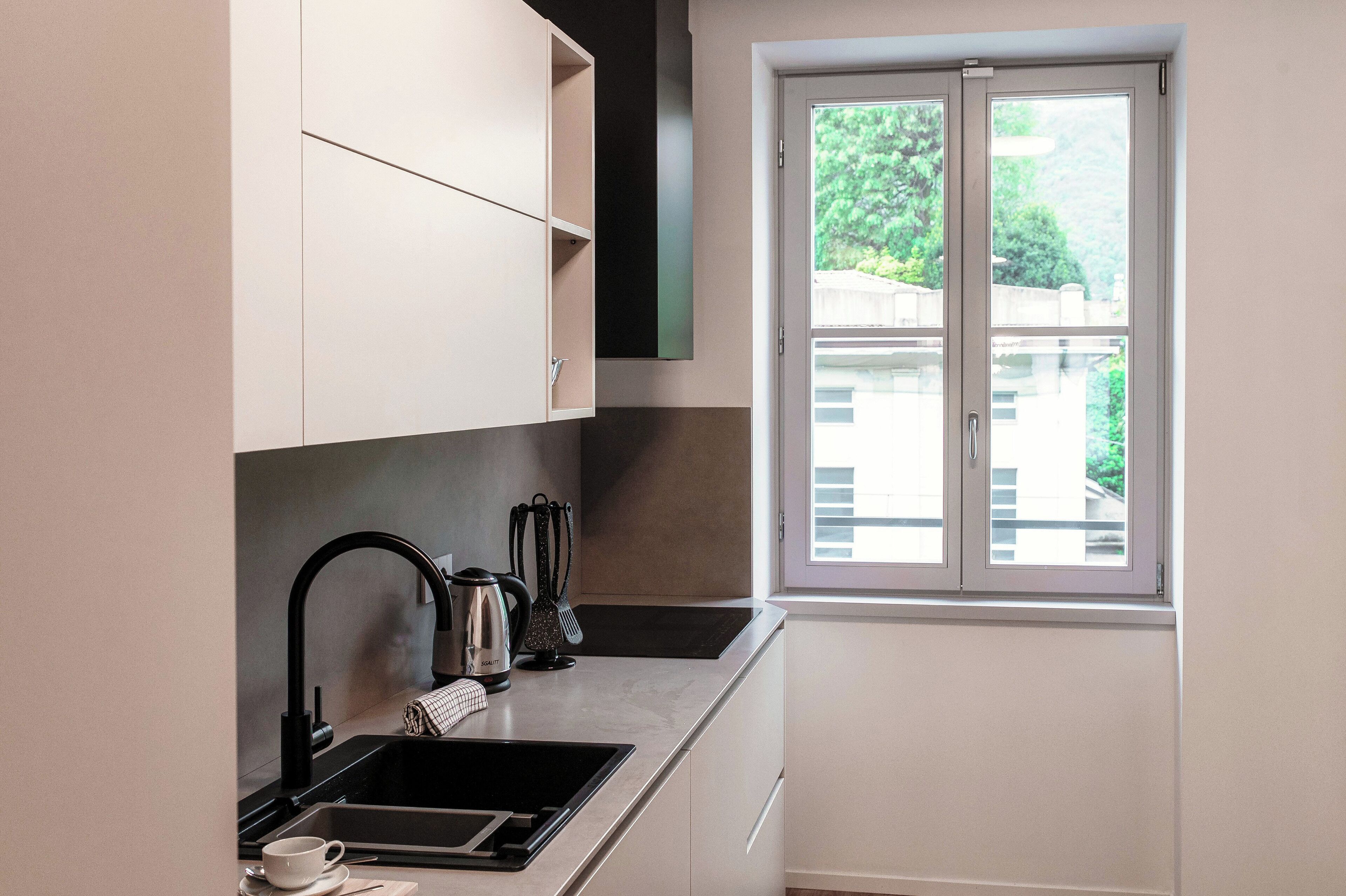 Una cocina moderna con un grifo negro, un lavamanos de acero inoxidable y una ventana con vistas a la vegetación.
