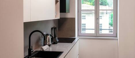 Una cocina moderna con un grifo negro, un lavamanos de acero inoxidable y una ventana con vistas a la vegetación.