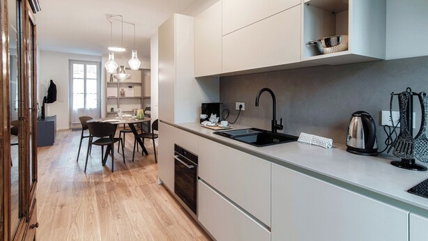 A modern kitchen with white cabinets, a black sink, and a dining area with a table and chairs. - Marinetti Suite 8 (Como)