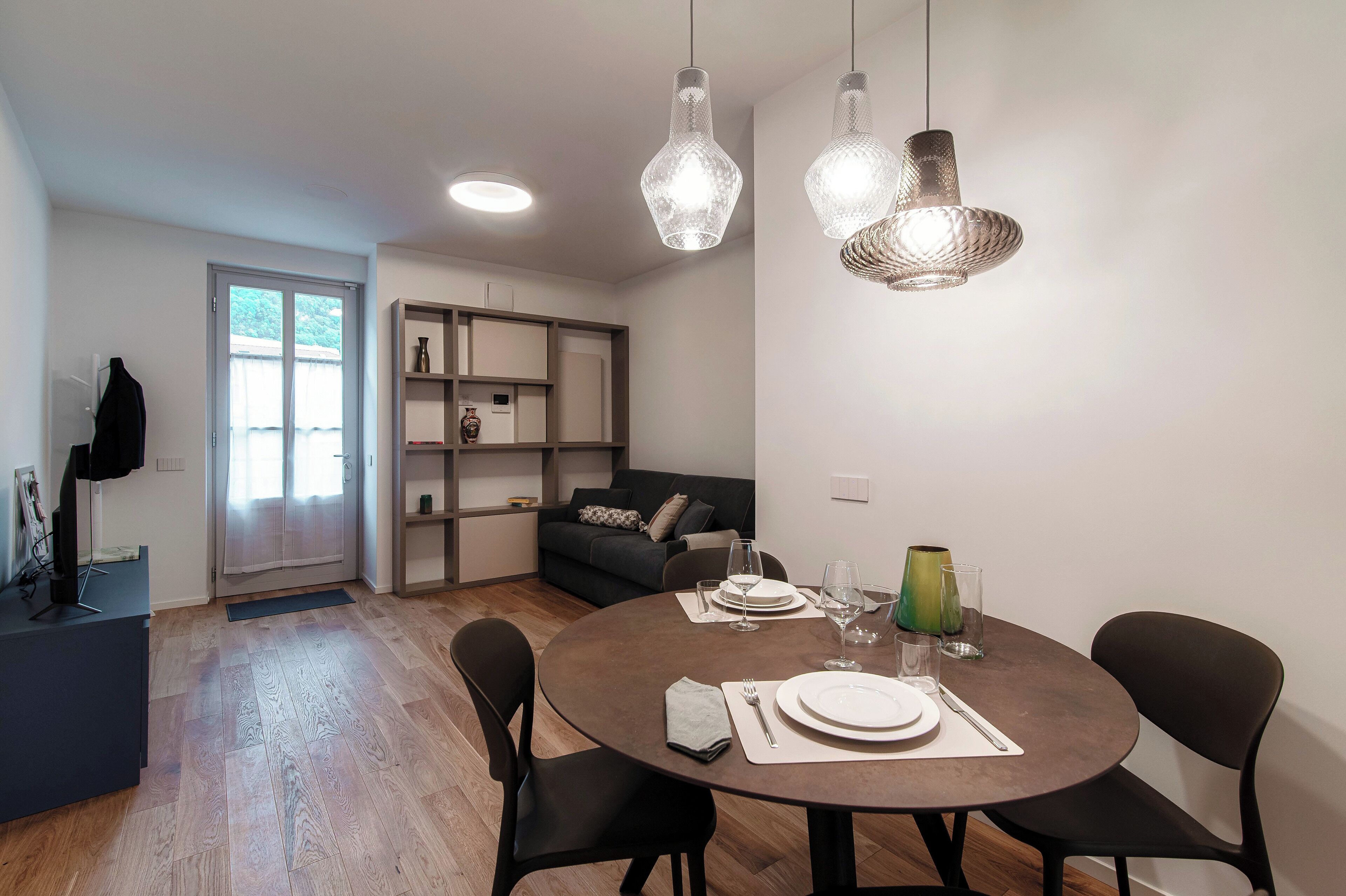 Een moderne eetruimte met een ronde tafel, zwarte stoelen en hangende pendantlampen.