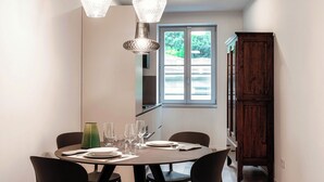 A dining area with a round table set for four, two hanging pendant lights, and a view of the outdoors through a window. - Marinetti Suite 8 (Como)