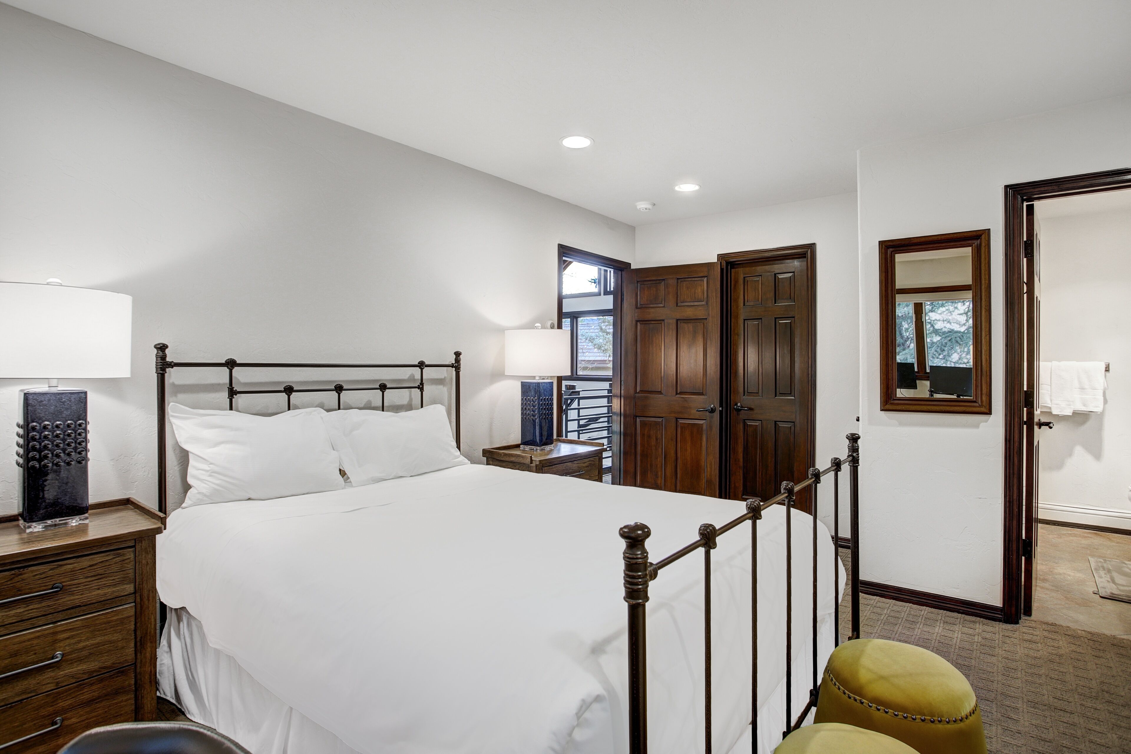 A bedroom with a large bed, wooden wardrobe, and a small table with a lamp.