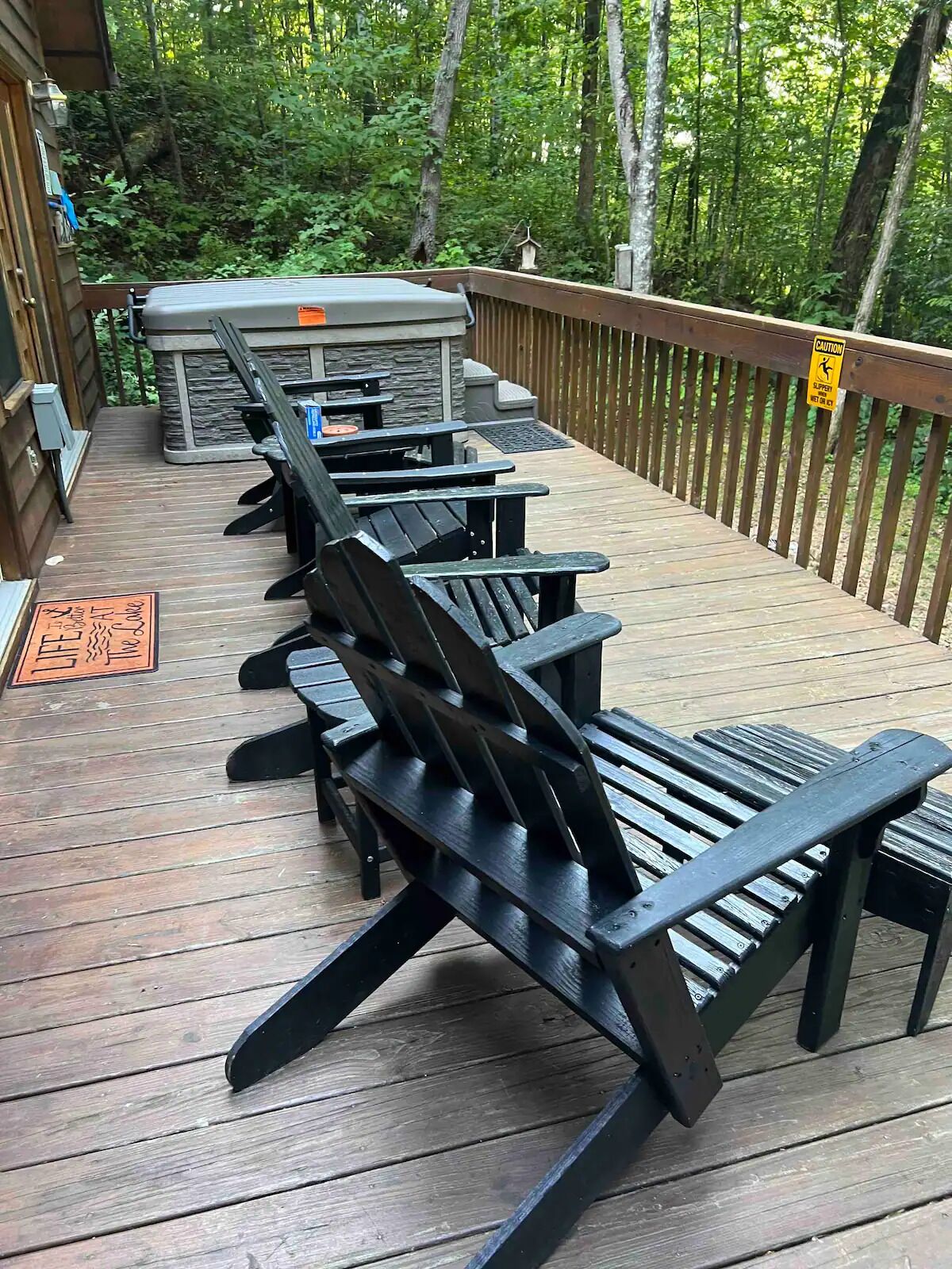 Une terrasse en bois avec des fauteuils Adirondack noirs et un barbecue.