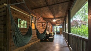 Eine Holzhütte mit einer Hängematte an der Decke, einer Holzterrasse und Blick auf grüne Umgebung.