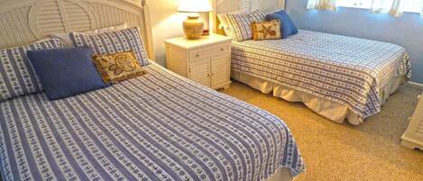 A bedroom with two beds, each with patterned bedding, a nightstand with a lamp, and a wall decoration.