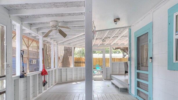 A covered porch with white wooden railings, a ceiling fan, and a view of a backyard.