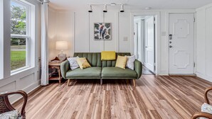 A room with a green sofa, wooden flooring, a lamp, a framed picture, and a door.