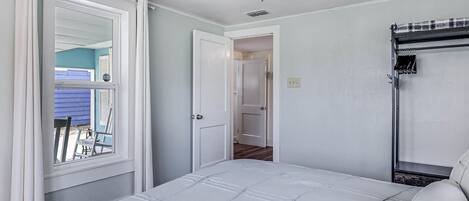 Un dormitorio con una cama, ventilador de techo, ventana con cortinas y puerta que da a otra habitación.